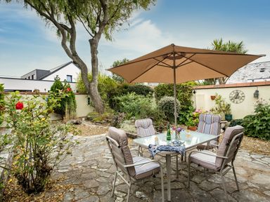 An outdoor patio with a glass table and cushioned chairs under a large umbrella in a garden at Longhouse Bungalow in Rock