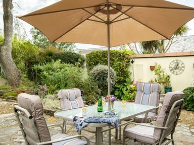 A patio table with four cushioned chairs under a large umbrella in a garden at Longhouse Bungalow in Rock
