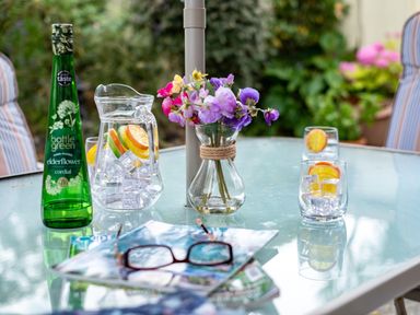 A glass patio table with a flower vase pitcher of water with ice and citrus cordial bottle at Longhouse Bungalow in Rock