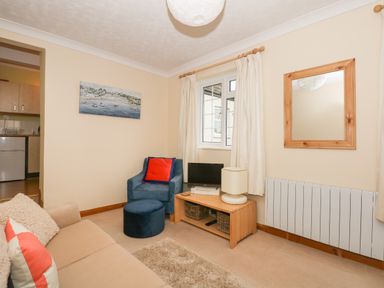 A sitting room with a beige sofa and blue armchair near a window with curtains and a wooden TV stand at 16 Norfolk Heights Docking