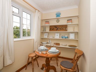 A dining area with a small round wooden table set for two and wooden chairs near shelves with decorative items at 16 Norfolk Heights in Docking