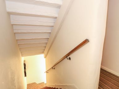 A narrow staircase with a wooden handrail and striped carpet at 16 Norfolk Heights in Docking