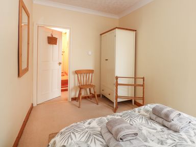 A bedroom with a bed holding folded towels a wooden chair a white wardrobe a wooden rack and a wall mirror at 16 Norfolk Heights in Docking