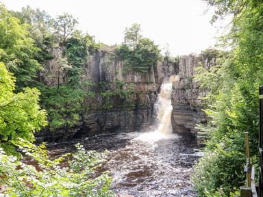 A waterfall flowing into a river surrounded by cliffs and green trees at Foxes Den in Winston near Staindrop