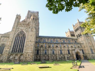 Exterior view of a large historic cathedral with stone walls and arched windows with grass and stone slabs in front at Foxes Den in Winston near Staindrop