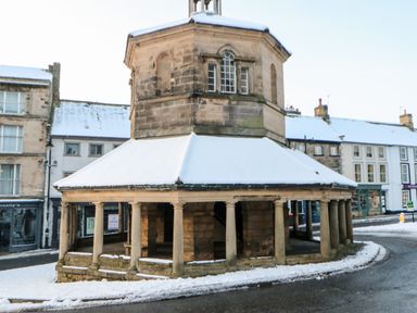 A historic stone market cross with a snow-covered roof and columns on a street corner in a small town