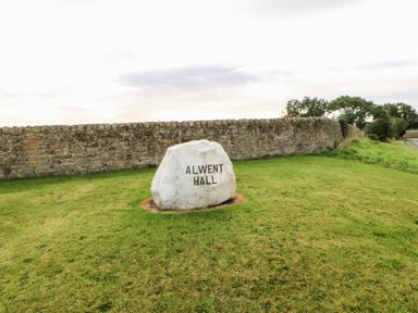 A white stone with Alwent Hall inscription on grass near a stone wall and trees at Foxes Den in Winston near Staindrop
