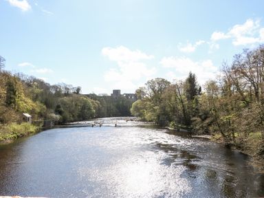 A river flowing through a wooded area with a stone ruin in the distance at Foxes Den in Winston near Staindrop