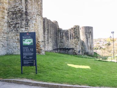 A stone castle wall with a sign providing information about Barnard Castle on a grassy area at Foxes Den in Winston near Staindrop