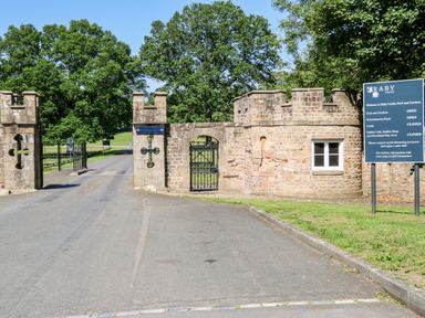 The entrance gate to Raby Castle with stone walls and a sign displaying opening information at Raby Castle in Winston near Staindrop