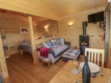 A wooden interior with a sofa bed and ottoman a bed in a corner a fireplace a dining table with a bottle and glass at Foxes Den in Winston near Staindrop