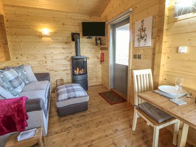 A wooden living room with a sofa ottoman wood stove dining table and chair at Foxes Den in Winston near Staindrop