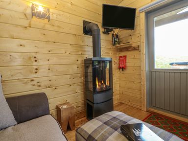 A room with a wood burning stove a TV on the wall a small wooden stool a sofa and a plaid ottoman at Foxes Den Winston near Staindrop