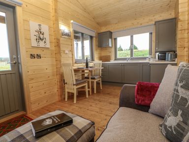 A kitchen and dining area with wooden walls and ceiling a small table with two chairs a sofa with cushions and a blanket at Foxes Den Winston near Staindrop