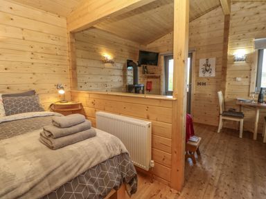 A wooden room with a bed and towels folded on it a small table and chair and a television at Foxes Den in Winston near Staindrop