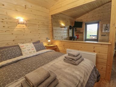 A bedroom with a bed linens and towels on the bed and wood paneled walls at Foxes Den in Winston near Staindrop