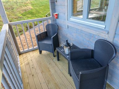 A small wooden balcony with two black wicker chairs and a table holding a bottle in a metal bucket and two glasses at Foxes Den in Winston near Staindrop