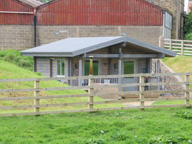 A small wooden cabin with a fenced grassy area in front at Foxes Den Winston near Staindrop