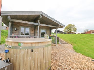 A wooden cabin with a hot tub and gravel path in a grassy area at Foxes Den in Winston near Staindrop