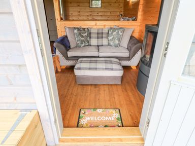 An entrance showing a welcome mat leading to a living area with a sofa and ottoman in a wooden cabin at Foxes Den Winston near Staindrop
