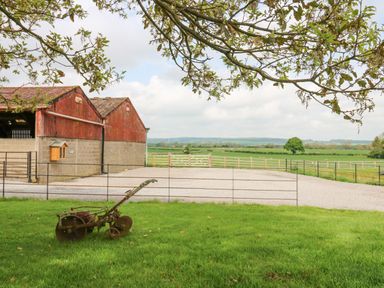A farmyard with an old plow on grass and red barns with fields in the background at Foxes Den in Winston near Staindrop