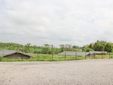 A gravel area with a metal fence overlooking rooftops and green fields at Foxes Den in Winston near Staindrop