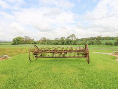 An old rusty farm machine on grass with wooden fences and trees in the background at Foxes Den Winston near Staindrop