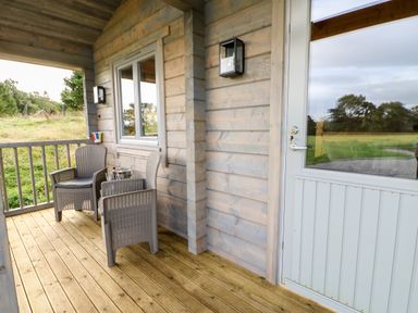 A wooden porch with two chairs a table and a glass door at Otters Holt in Winston near Staindrop