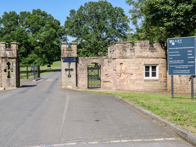 The entrance gate and stone wall to Raby Castle with a sign showing opening times and trees in the background at Otters Holt in Winston near Staindrop