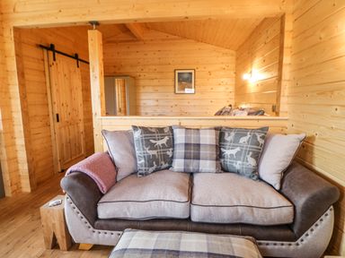 A wooden living room with a sofa and cushions and a sliding door at Otters Holt in Winston near Staindrop