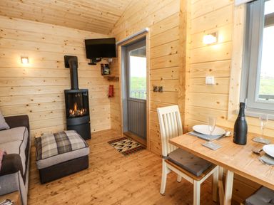 A wooden interior room with a dining table set with plates and glasses a chair a sofa a lit stove and a wall-mounted television at Otters Holt in Winston near Staindrop