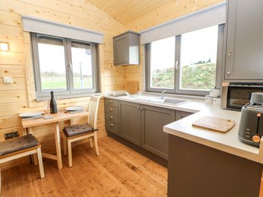 A kitchen with gray cabinets a wooden dining table with two chairs and windows showing outdoor greenery at Otters Holt in Winston near Staindrop