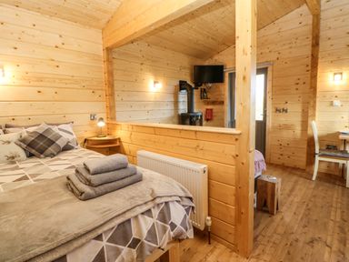 A bedroom with a bed folded towels and a wood burning stove in a wooden cabin at Otters Holt Winston near Staindrop