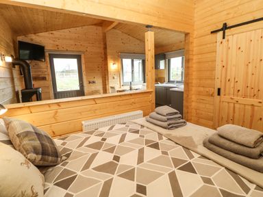 A bedroom with a patterned bedspread and folded towels overlooking a wooden interior with kitchen and dining area at Otters Holt in Winston near Staindrop