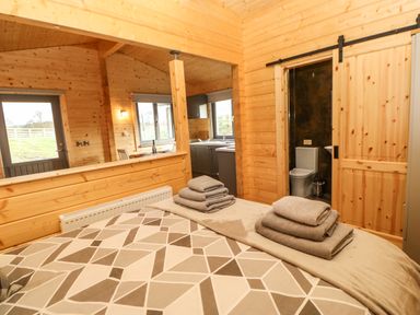 A bedroom with a bed and folded towels a sliding wooden door leading to a bathroom and a view into a kitchen at Otters Holt in Winston near Staindrop