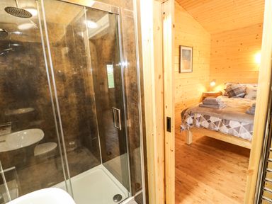 A bathroom with a glass shower and a bedroom with a bed and bedside table at Otters Holt in Winston near Staindrop