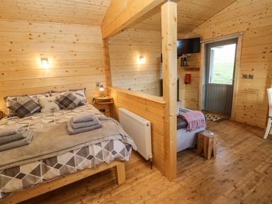 A wooden room with a bed folded towels a small sofa a wooden stool a television and a door at Otters Holt Winston near Staindrop