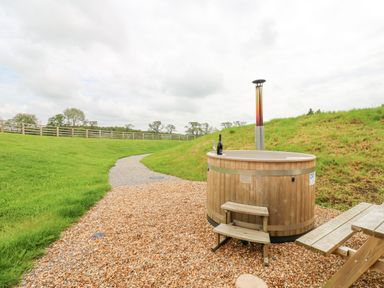 A wooden hot tub with steps and a picnic table on gravel next to a grassy path at Otters Holt in Winston near Staindrop