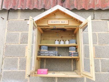 A wooden honesty box mounted on a stone wall with jars of honey instant grills firelighters and a pink cash box inside at Otters Holt in Winston near Staindrop