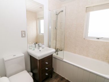 A bathroom with a toilet sink with cabinet and bathtub with shower at Sunstone Lodge Garreg Haul Lodge in Cilan near Abersoch