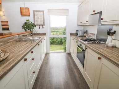 A kitchen with wooden countertops and white cabinets with a window at the end showing a garden at Sunstone Lodge Garreg Haul Lodge Cilan near Abersoch