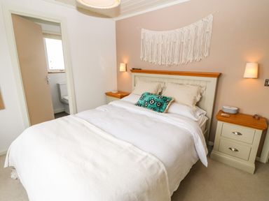 A bedroom with a double bed between two bedside tables and a bathroom visible through an open door at Sunstone Lodge Garreg Haul Lodge Cilan near Abersoch