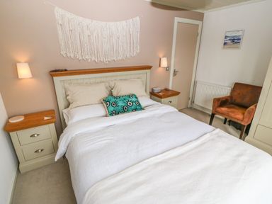 A bedroom with a bed, two bedside tables, a brown armchair and a wall hanging at Sunstone Lodge Garreg Haul Lodge in Cilan near Abersoch