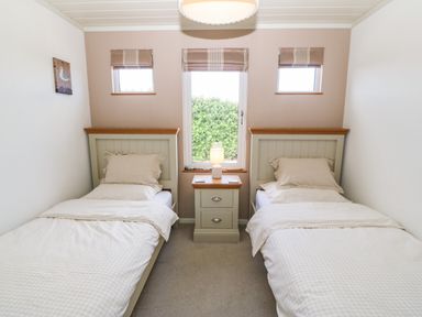 A bedroom with two single beds separated by a bedside table with a lamp at Sunstone Lodge Garreg Haul Lodge in Cilan near Abersoch