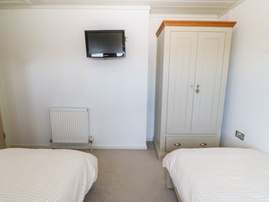 A bedroom with two single beds a wardrobe a wall-mounted TV and a radiator at Sunstone Lodge (Garreg Haul Lodge) in Cilan near Abersoch