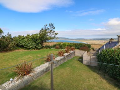 A garden with plants and grass overlooking a coastline and hills at Sunstone Lodge (Garreg Haul Lodge) in Cilan near Abersoch