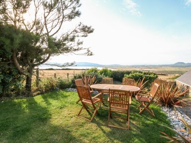 A garden with a wooden table and chairs overlooking fields and hills at Sunstone Lodge Garreg Haul Lodge in Cilan near Abersoch