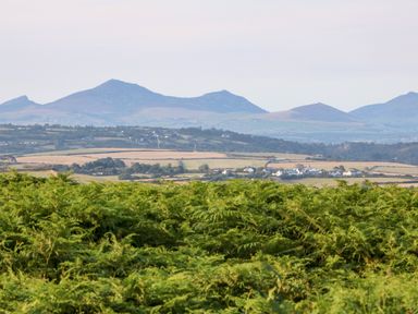 A landscape with green bushes in the foreground fields and houses in the middle and hills in the background at Sunstone Lodge Garreg Haul Lodge in Cilan near Abersoch