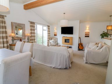 A living room with sofas chairs a guitar and a television mounted on a wall at Sunstone Lodge Garreg Haul Lodge Cilan near Abersoch