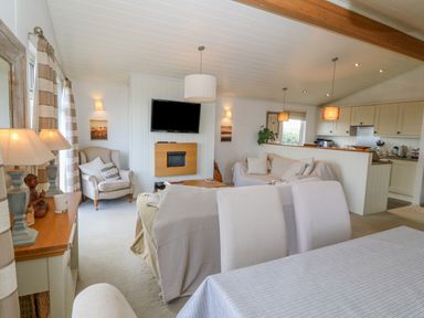 An open living room and kitchen area with sofas a TV wall unit dining table and chairs at Sunstone Lodge Garreg Haul Lodge Cilan near Abersoch